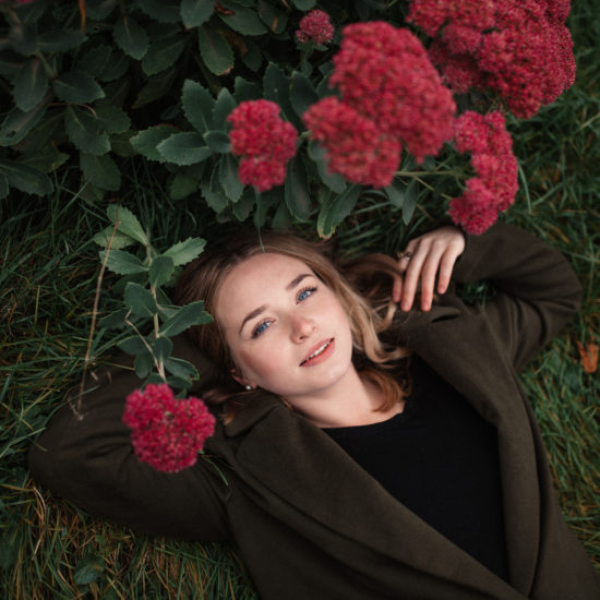 A woman is lying on the grass with red flowers on her