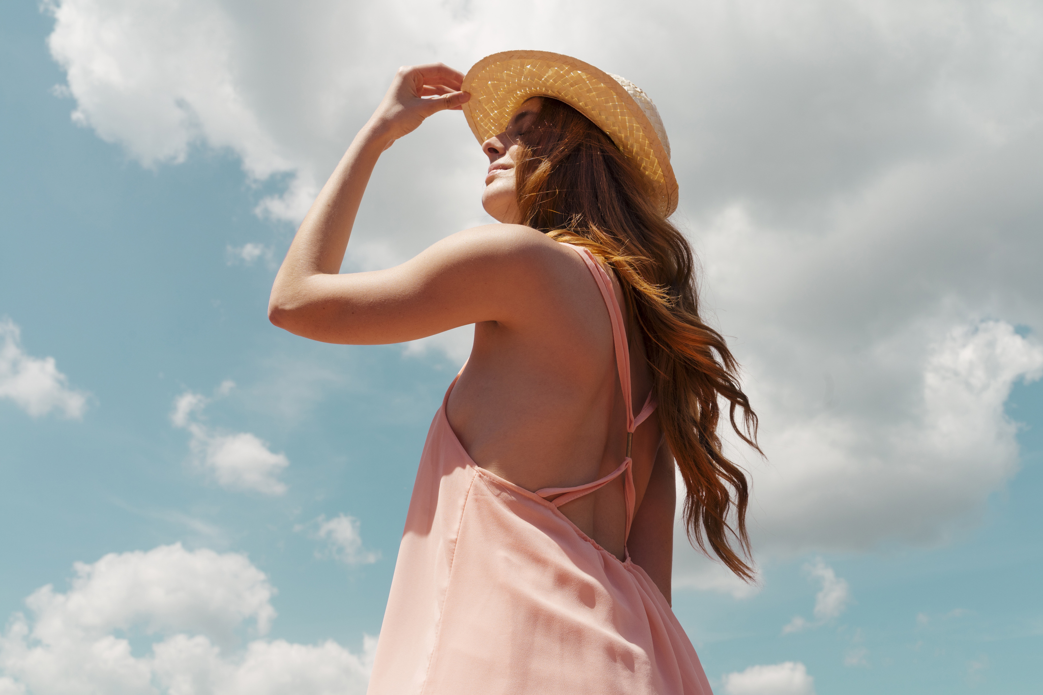 Woman with pink dress and straw hat with cloudy sky background