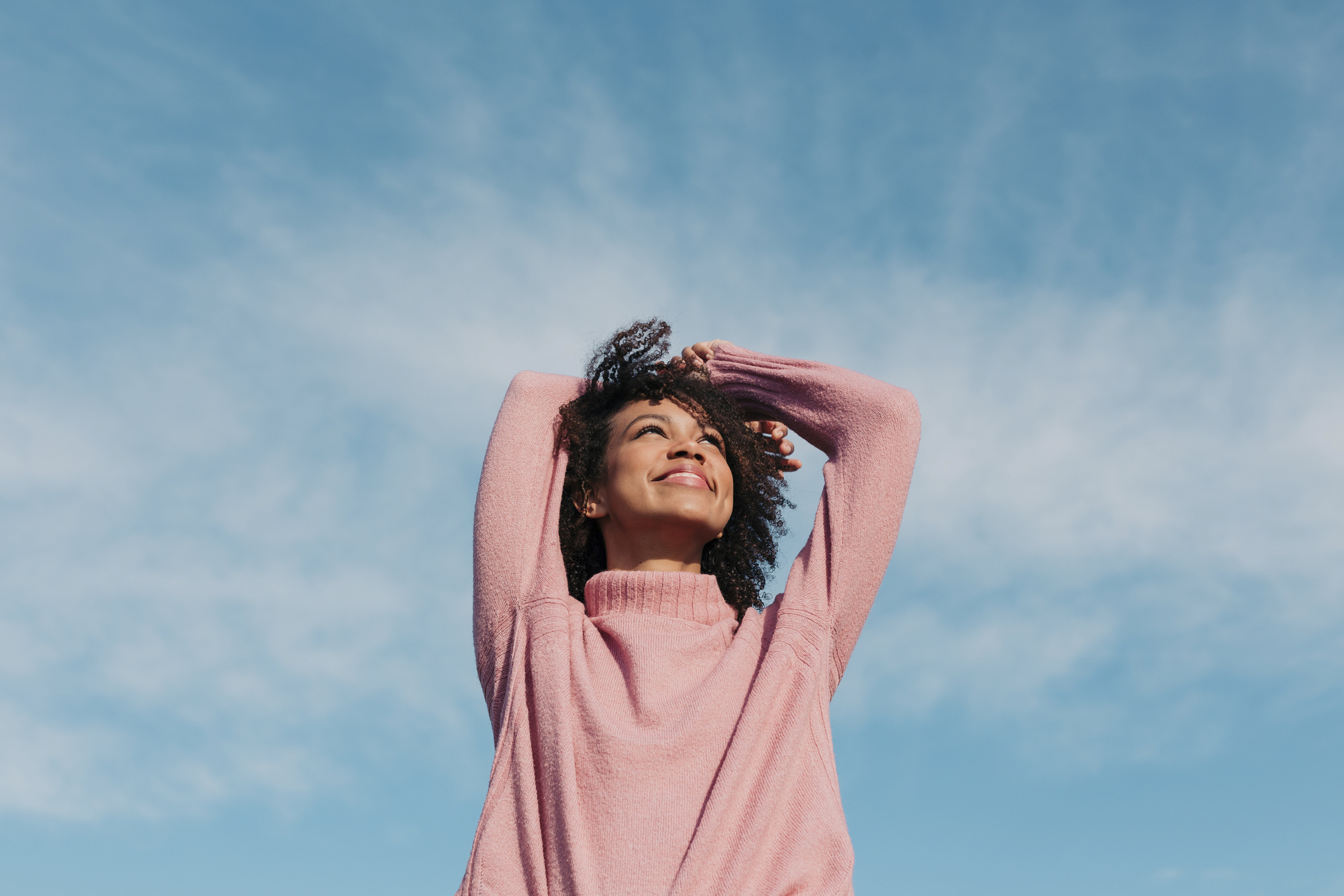 A woman in a pink sweater looks to the sky and smiles