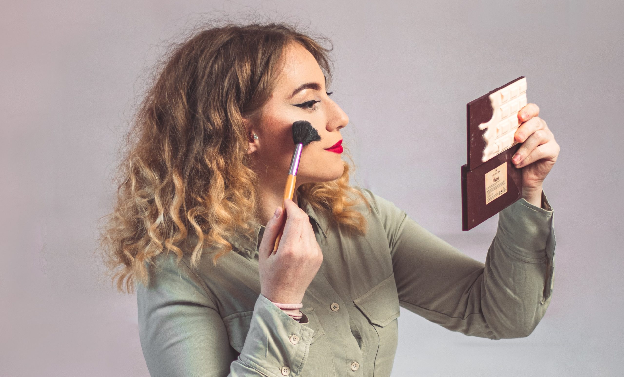 A girl with curly blond hair is applying makeup