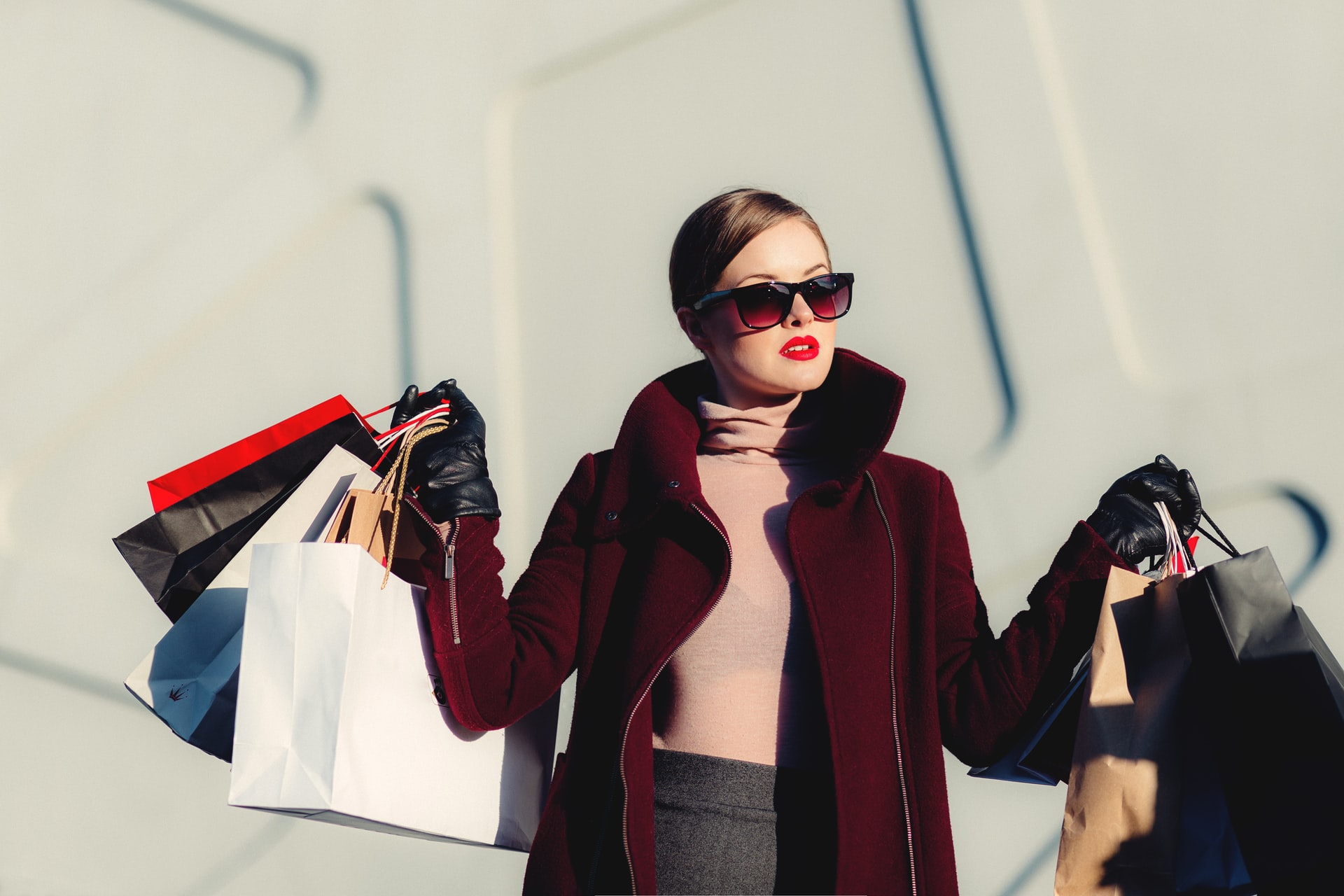 A woman in a red coat and sunglasses is holding shopping bags