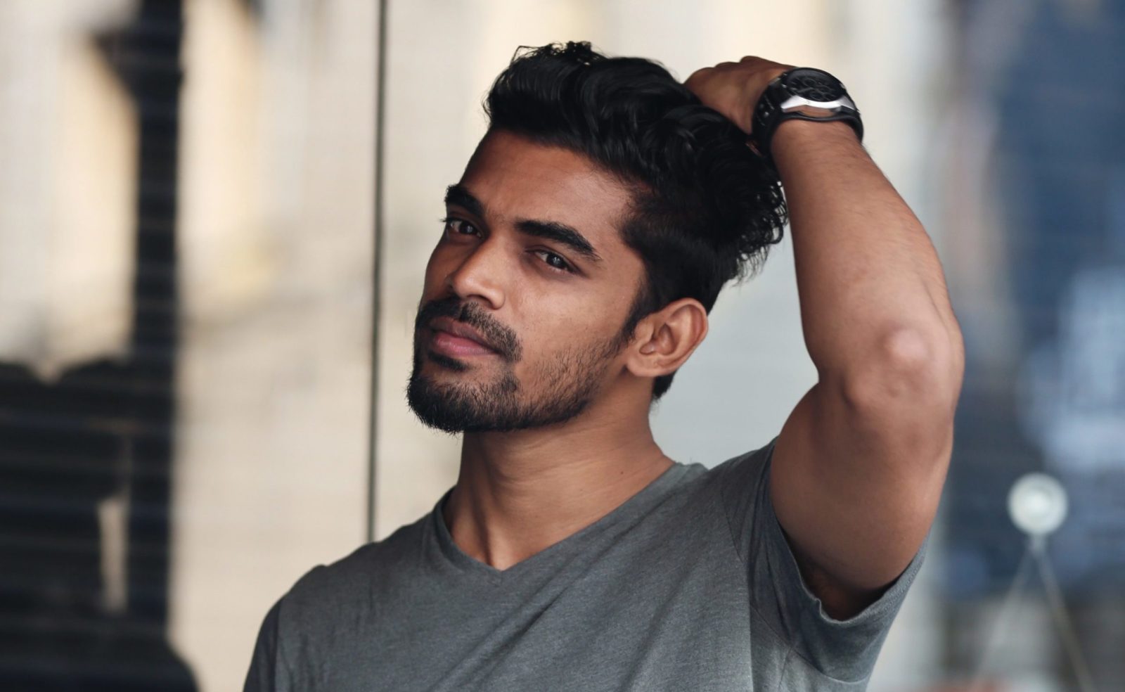 A man with a gray shirt and a watch is looking at the camera