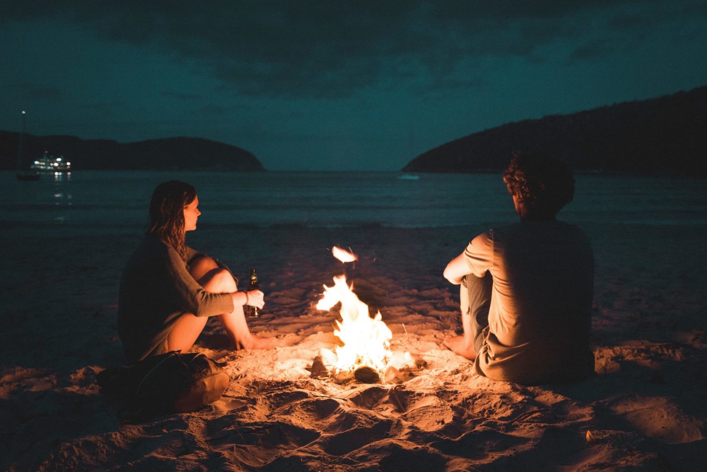 A man and a woman make a bonfire on the beach at night