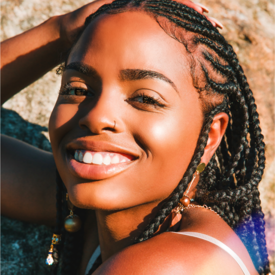 A woman with braids and a nose ring smiles at the camera with a filter