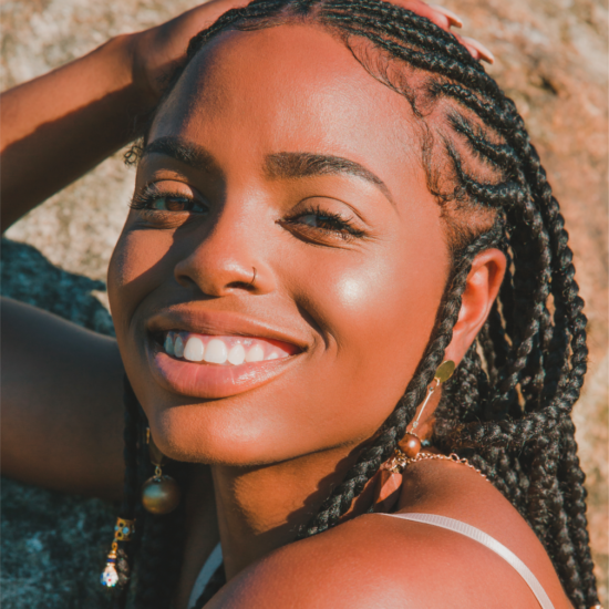 A woman with braids and a nose ring smiles at the camera